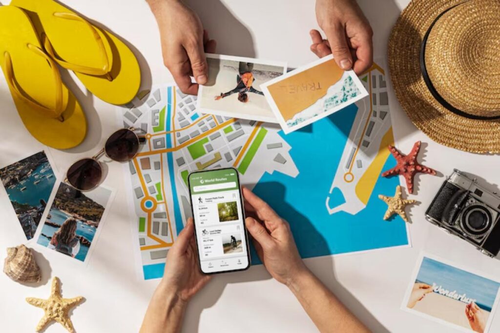 Hands holding postcards and a smartphone on a travel map, surrounded by sunglasses, flip-flops, a camera, and beach-themed items.