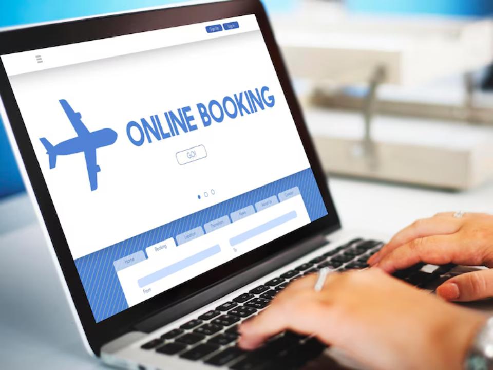  A person typing on a laptop displaying an online booking website featuring an airplane graphic and search fields.