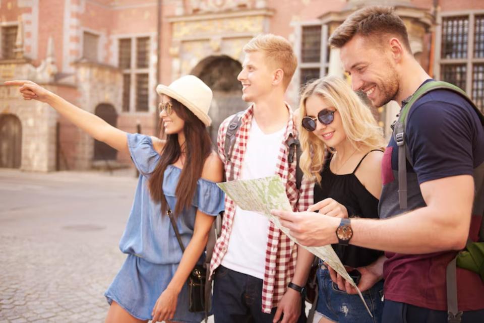  A group of young adults stands outdoors, studying a map together, with one person pointing towards a direction in an urban setting.