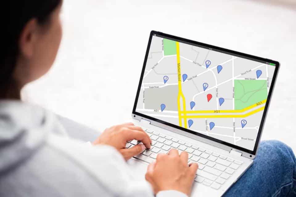 A person using a laptop to view a digital map, displaying various location markers and streets, while seated indoors.