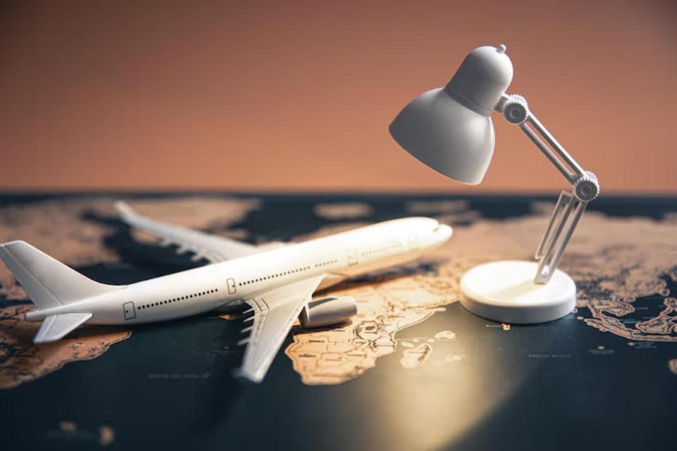  A white airplane model and a sleek desk lamp rest on a world map, against a warm, neutral background.