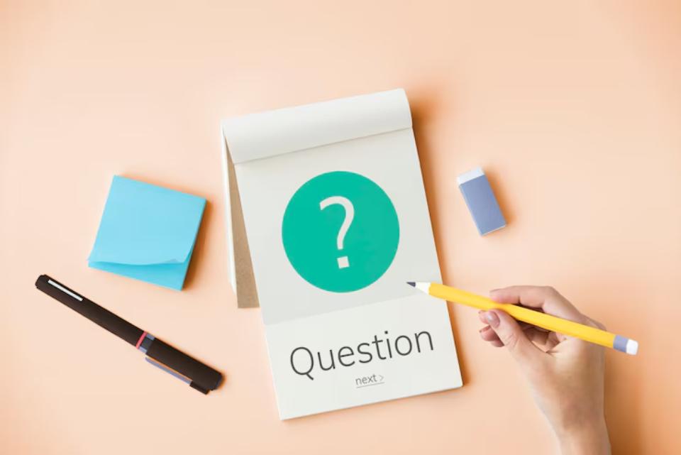A hand holding a yellow pencil points to a notepad displaying a question mark and the word Question,surrounded by stationery on a pastel background.