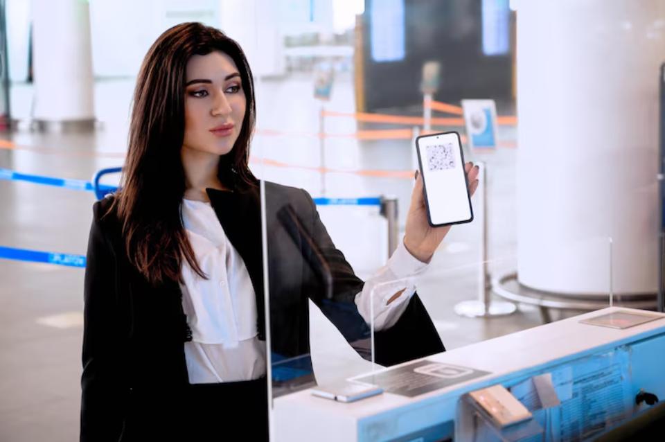  A woman in a black suit holds a smartphone displaying a digital QR code at an airport check-in counter.