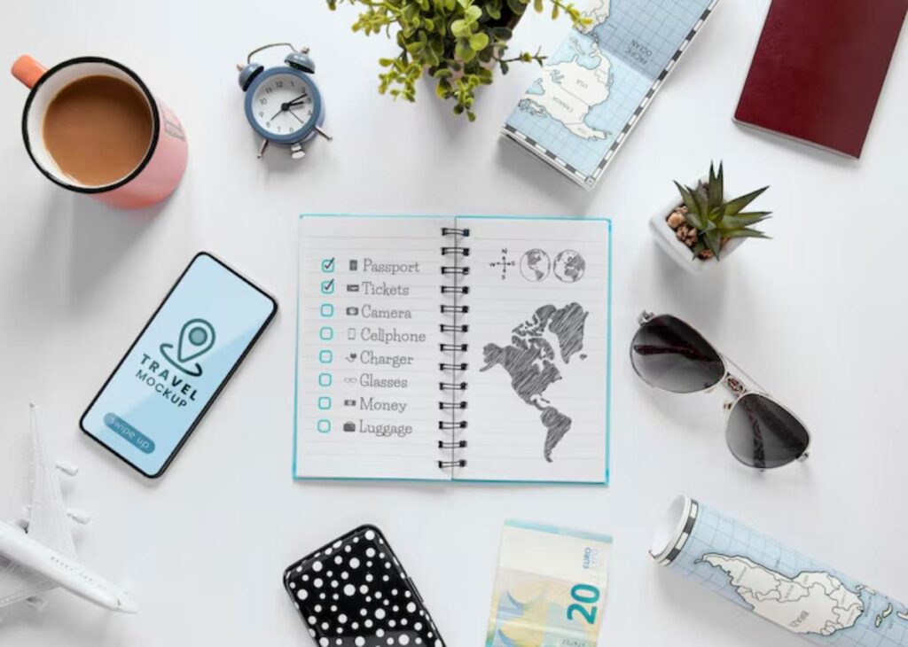A flat lay of travel essentials: coffee, phone, notebook with a checklist, money, sunglasses, and a globe-themed travel mug.