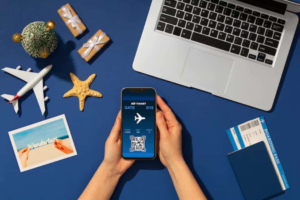 A person's hand holds a smartphone displaying a digital boarding pass, surrounded by travel items on a blue background.