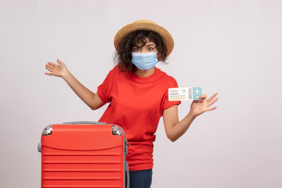  AA person in a red shirt and straw hat poses with a red suitcase and a boarding pass, conveying excitement for travel.
