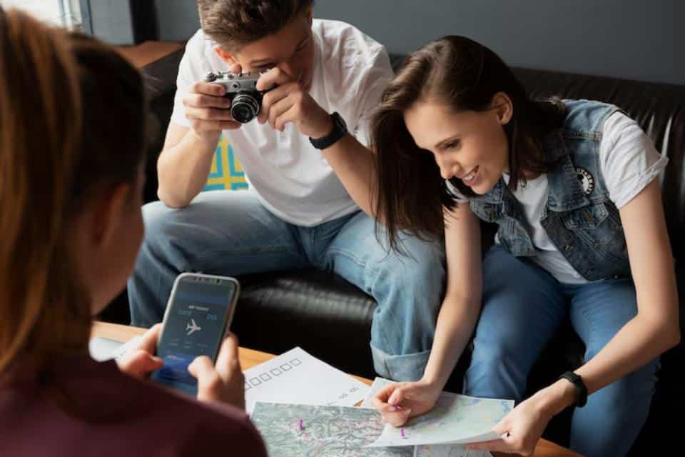 A group of friends studies a map and checks travel details on a phone, planning their next adventure in a cozy living room.
