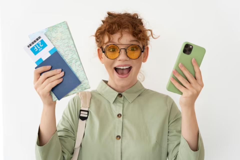 A person in a green shirt holds a phone in one hand and travel documents, including a map and a boarding pass, in the other.