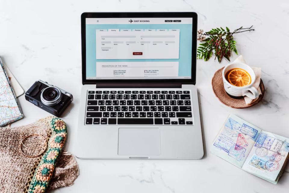 Aerial view of a map, laptop, camera, and hands planning a journey with a cup and notebook on a wooden table.